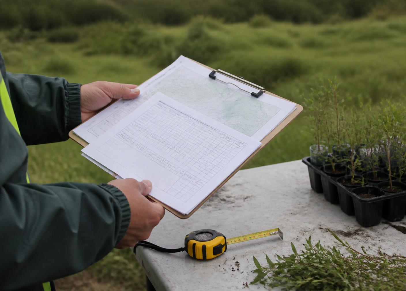 Gestor ambiental analisando formulários técnicos e mapa topográfico em prancheta durante vistoria de campo